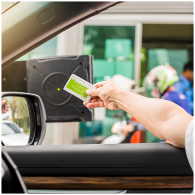 Uma pessoa com o braço para fora do carro, segurando um cartão para pagar o estacionamento